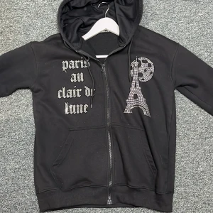 Svart rhinestone hoodie från Blinglucid - Snygg svart hoodie med dragkedja från Blinglucid. Den har en rhinestone text på tröjan och är i väldigt bra skick.