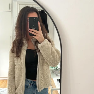 Beige teddyjacka från H&M SLUTSÅLT ÖVERALLT  - Mysig beige teddyjacka från H&M som inte kom till användning mer, med dragkedja framtill. Jackan har en fluffig textur och långa ärmar, jag har storleken Xs på koftor men jackan är köpt från barnavdelningen eftersom att ja tyckte den va så fin använd, så ni som har storleken xs denna jackan kommer att fungera på er,  (jackan är helt slutsåld överallt)