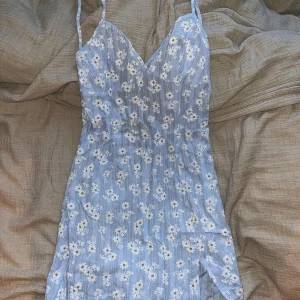 Blommig klänning från Shein - Söt ljusblå klänning med blommigt mönster från Shein. Klänningen har smala axelband och en v-ringad design. Perfekt för varma dagar med sin lätta och luftiga stil.