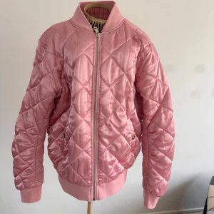 Rosa quiltad bomberjacka från BikBok - Säljer en snygg rosa och glansig  bomberjacka från BikBok med quiltat mönster. Jackan har dragkedja framtill och fickor. Perfekt för att ge din outfit en färgklick! Stl L