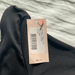 Svart långärmad topp från Nelly - Säljer en topp med knytdetalj vid ryggen.  Perfekt för en stilren look. Toppen har en figurnära passform och är tillverkad i ett mjukt material. Den är helt ny.