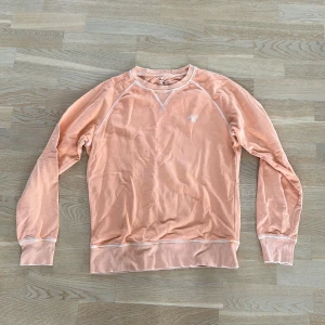 Persikofärgad tröja från GANT - Säljer en stilren persikofärgad tröja från GANT. Tröjan har långa ärmar och en klassisk rund halsringning med dekorativa sömmar. Perfekt för en avslappnad och bekväm stil. Använd några få gånger men i bra skick och storlek S. 