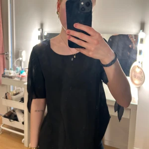 Svart blus från Shein - Säljer en svart blus från Shein med korta ärmar och dekorativa knytband på sidorna. Perfekt för en stilren look. Blusen har en rund halsringning och är tillverkad i ett lätt material.💞