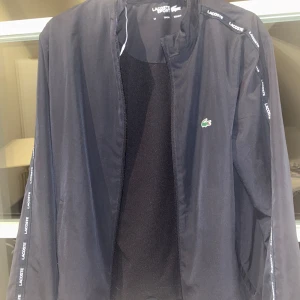 Lacoste tracksuit  - Snygg lacoste tracksuit med lacoste på armarna, matchande byxor storlek 164 men passar även xs. Mycket bra skick inga tecken på användning 