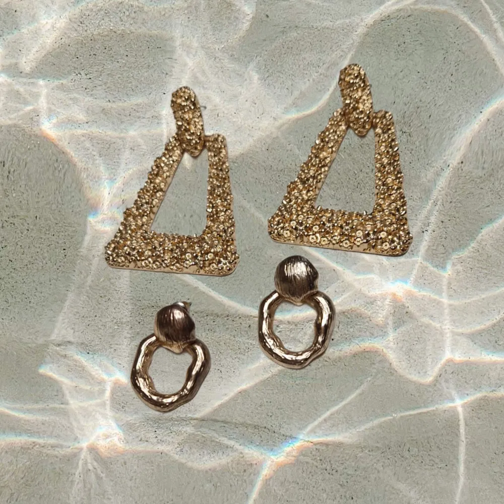 Säljer två par örhängen. Ett par är triangelformade i guld med glittriga detaljer som saknar pluppar, och det andra paret är i mörkare guld med en organisk, vriden form. Perfekta för att ge en touch av glamour till din outfit.. Asusteet.