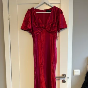 Röd klänning  - Snygg röd klänning från Little Mistress. Den har korta ärmar och en v-ringad design med knytning framtill. Perfekt för en festlig kväll eller bal. Aldrig använd 