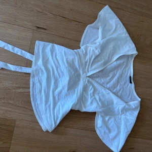 Vit omlottopp med knytband - Säljer en vit omlottopp med v-ringning och korta, lite fladdriga ärmar. Toppen har knytband i midjan som ger en snygg passform. 