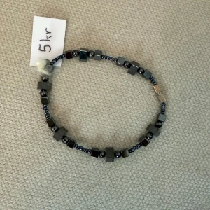 Armband - Stilrent armband med små svarta och silverfärgade pärlor i både kubisk och rund form. Pärlorna är trädda på en tunn tråd och ger ett coolt, minimalistiskt intryck. Perfekt för dig som gillar diskreta accessoarer med en twist.