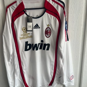 AC Milan långärmad Kaka Champions League tröja - Säljer en officiell AC Milan långärmad fotbollströja från Champions League-finalen 2007 med Kaka och nummer 22 på ryggen. Tröjan är vit med röda och svarta detaljer, Adidas-logga, klubbmärke och Champions League-patch på ärmen. Materialet är lätt och ventilerande polyester.