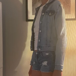 Ljusblå jeansjacka - Snygg ljusblå jeansjacka med croppad passform och klassiska knappar framtill. Jackan har långa ärmar och stilrena sömmar som ger en cool vibe. .