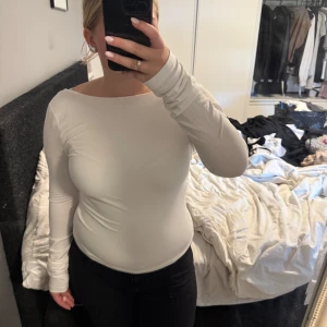 Vit långärmad topp med öppen rygg - Säljer en vit långärmad topp med snygg öppen rygg och bred halsringning. Modellen är tight och sitter riktigt snyggt på kroppen. Materialet är mjukt och stretchigt, troligen bomull med lite syntet. Perfekt för dig som gillar stilrena och enkla plagg med en twist.