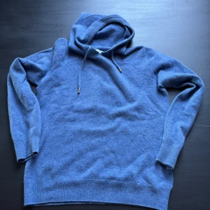 Blå merinoull hoodie - Blå hoodie i merinoull med huva och snörning. Trjöan är i st xxs men passar xs bra. Perfekt för kyliga dagar när du vill vara både bekväm och snygg. Tveka inte att höra av dig:)
