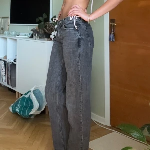 Mörkgråa lågmidjade straight jeans - Säljer ett par mörkgråa jeans. Dom är lite för korta och lite tighta i midjan för min smak. Jag som är på bilden är nästan 184cm och får dra lite för att stänga. Det står strl 38 i jeansen men jag skulle verkligen säga att det är 36 då exempelvis de andra blåa gina jeansen jag säljer också är i storlek 38 men alldeles för stora istället.  