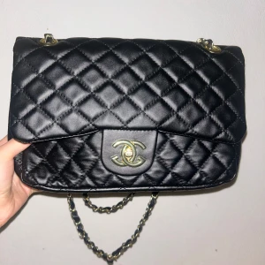 Svart axelväska - Snygg svart axelväska med klassiskt mönster och guldfärgade detaljer. Väskan har en kedjerem med inslag av svart skinn och ikonisk CC-logga på framsidan. Perfekt storlek för det viktigaste och en riktig statement piece. Pris kan diskuteras vid snabb affär 