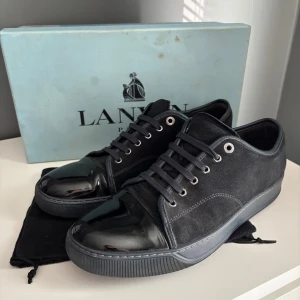 Lanvin  - Snygga mörkablåa sneakers från Lanvin med en cool mix av mocka och lackad skinn på tån. Skorna har rund tå, platt sula och svarta snören med metallöglor. Insidan är fodrad med mjukt skinn för extra komfort. Perfekt för dig som gillar stilrena och lyxiga detaljer. Uk 10