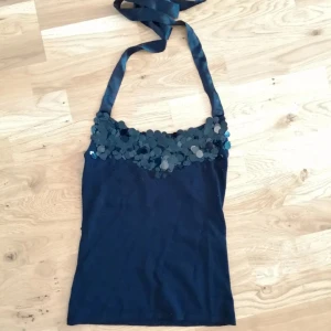 Svart paljettprydd linnetopp - Svart linnetopp med breda axelband i satin och massor av glittrande paljetter längs överdelen. Snygg och figurnära passform. Materialet känns mjukt och stretchigt. Passar XS-S.