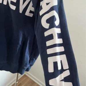 Mörkblå mjukisset med tryck - Säljer ett mörkblått mjukisset med stora vita tryck längs benen och ärmarna där det står 'IMAGINE BELIEVE ACHIEVE'. Byxorna har en avslappnad passform och är gjorda i mjukt bomullsmaterial, perfekta för chill dagar eller träning.