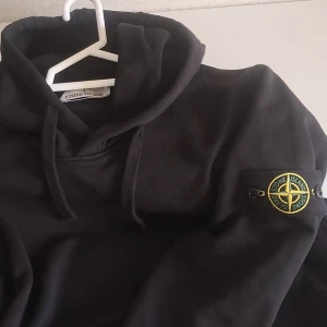 Svart hoodie från Stone Island - Black hoodie from Stone Island with classic logo patch on the sleeve. The sweatshirt has a hood with drawstring and is made of 100% soft cotto.. Brand new, never worn. No tags or original packaging, but in perfect condition. Carefully stored and ready to ship. 🔴🔴 NEW PRICE: 3 500KR (NK Gbg) 🔴🔴 