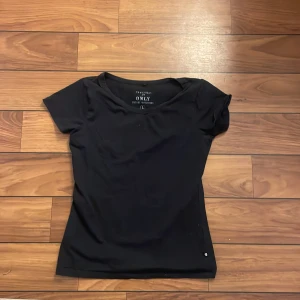 Svart topp från ONLY - En stilren svart topp från ONLY med rund halsringning har lite små fläckar på framsidan. Den ser lite grön ut på andra bilden men är helt svart.  Den sitter dock som en smal och inte som en L.