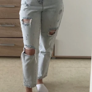 Ljusa ripped jeans med raka ben - Säljer ett par ljusa jeans med raka ben och flera snygga slitningar och hål på framsidan. Jeansen har en klassisk femficksdesign och är croppade vid anklarna. Perfekta för dig som gillar en avslappnad och trendig streetstil.