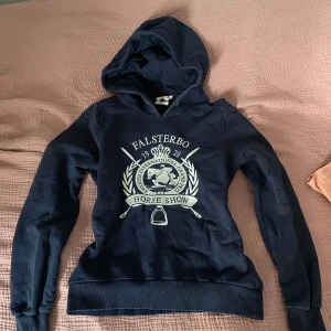 Mörkblå hoodie Falsterbo Horse Show - Snygg mörkblå hoodie från Gina Tricot med Falsterbo Horse Show-tryck i vitt och beige på bröstet. Liten i storleken, mer en XS/S! Tröjan har huva, långa ärmar och ribbade muddar.