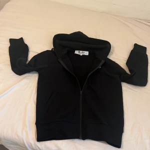 Svart hoodie Comme des Garçons Play S - Svart hoodie från Comme des Garçons Play i storlek S. Tröjan har dragkedja framtill, huva och ett stort svart hjärta med ögon på ryggen. Tillverkad i 100% bomull, med ribbade muddar och fickor på sidorna. Perfekt för dig som gillar streetwear och ikoniska prints. Sitter mer som en xs