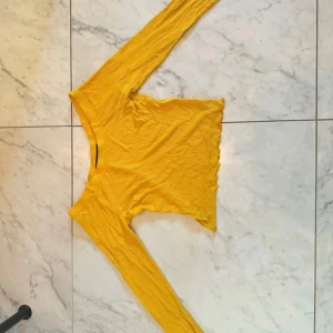 Gul långärmad topp från Bik Bok - Säljer en gul långärmad topp från Bik Bok i storlek XS. Modellen är croppad med vågig kant nedtill och har en rund halsringning. Materialet är mjukt och stretchigt med ribbad struktur, tillverkat av 95% viskos och 5% elastan. Perfekt för dig som gillar färg och vill sticka ut.