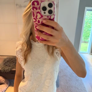 Vit spetsblus med korta ärmar - Supersöt vit blus med detaljerad spets och blommigt mönster. Blusen har ärmlös design med volangkant vid axlarna och en rund halsringning. Tröjan har enbart använts två/tre gånger och är därför i fantastiskt skick💕
