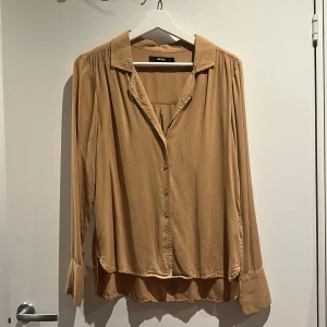 Beige skjorta från Bik Bok - Snygg beige skjorta från Bik Bok i storlek S. Skjortan har klassisk krage, knappar framtill och långa ärmar med breda manschetter.