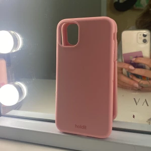 Rosa mobilskal från Holdit - Säljer en stilren rosa mobilskal från Holdit med mjuk och slät yta. Skalet har en enkel design utan mönster och passar perfekt till din iPhone. Färgen är ljusrosa och materialet känns som syntet, vilket ger ett skönt grepp i handen.