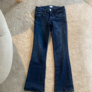 Bootcut jeans från Gina Tricot - Mörkblå bootcut jeans från Gina Tricot med klassisk femficksdesign och snyggt utställda ben. Jeansen har normal passform och är tillverkade i mjukt denimtyg med knapp och dragkedja framtill. Perfekta för dig som gillar retrovibbar och stilrena detaljer.