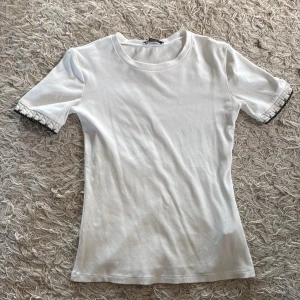Vit topp med spetsdetalj från Zara - Säljer en vit topp från Zara i storlek S. Den har korta ärmar med snygga spetsdetaljer och en rund halsringning. Materialet är mjukt och känns skönt mot huden, perfekt för dig som gillar stilrena plagg med en liten twist på ärmarna. Oanvänd o slutsåld.