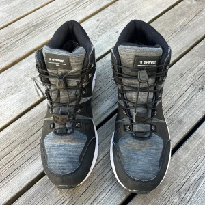 Svarta och grå sneakers från Everest - Snygga svarta och grå sneakers/kängor från Everest med högt skaft och vit sula. Skorna har snörning med snabblås, vattentätt material.  Perfekt för dig som gillar en sportig stil och vill ha skor som klarar regn och rusk.                    Innermått 24-24,5 cm Bara använda ett fåtal gånger , så de är i väldigt bra skick 