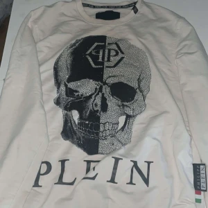 Vit långärmad tröja Philipp Plein - Säljer en vit långärmad tröja från Philipp Plein med ett stort svart döskalletryck och logga på bröstet. Tröjan har rund hals och är tillverkad i mjuk bomull. Snyggt statement-plagg med cool design och tydlig branding.