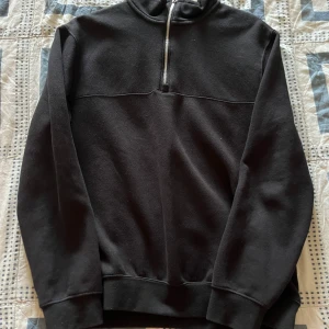Svart half zip hoodie - Svart hoodie med half zip-dragkedja och hög krage. Tröjan har långärmade ärmar och är gjord i mjukt material som känns skönt mot huden. Perfekt för chill dagar eller när du vill ha en enkel och stilren look.