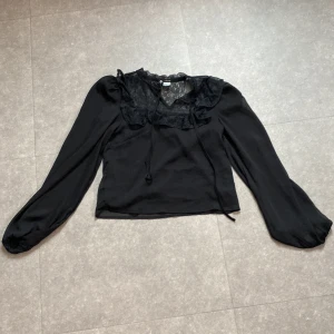 Svart blus med spets från H&M Divided - Supersnygg svart blus från H&M Divided i storlek XXS. Blusen har transparent spets upptill, v-ringad hals med knytband och långa puffiga ärmar med resår vid mudden. Dubbel tyg över överkroppen. Mycket bra skick💕