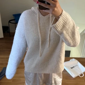 Mysig vit hoodie med huva - Supermysig vit hoodie med huva och snörning. Tröjan är stickad och har en loose passform med långa ärmar och ribbade muddar. Perfekt för chill dagar hemma eller när du vill vara extra comfy. Enkel och stilren design som passar till allt.