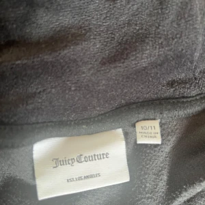 Svart tröja med dragkedja från Juicy Couture - Svart tröja från Juicy Couture i mjuk velour med huva och dragkedja. Jackan har ett broderat JC-logo på bröstet och snygga detaljer i silver vid dragkedjan. Använd 5-10 gånger. Bra skick!