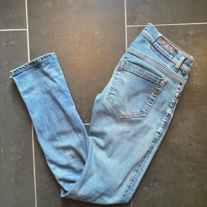 Dondup George - Säljer ett par ljusblå skinny jeans från dondup med coolt tryck och röd söm på bakfickan. Jeansen har klassisk femficksdesign, smal passform och är tillverkade i mjukt denimtyg. Perfekt för dig som gillar en clean och modern look.