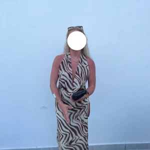 Zebramönstrad långklänning med öppen rygg - Säljer en snygg långklänning med zebramönster i beige och brunt. Klänningen har omlott framtill, djup v-ringning och är axelbandslös med öppen rygg! Klänningen är endast använd en gång!  