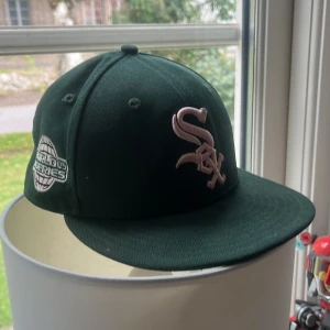 Mörkgrön White Sox keps från New Era - Snygg mörkgrön White Sox keps från New Era 59FIFTY med broderad logga i ljusrosa framtill och World Series-märke på sidan. Kepsen är tillverkad i 100% polyester och har en klassisk, rak skärm. Perfekt för dig som gillar baseball och streetwear.