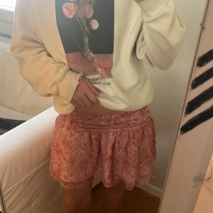 Rosa kortkjol med paisleymönster - Supersöt kortkjol i rosa med vitt paisleyinspirerat mönster. Kjolen har en flowy och lätt form med bred linning som sitter bekvämt i midjan. Perfekt för varma dagar och ger en chill och feminin vibe. Materialet känns mjukt och luftigt. 