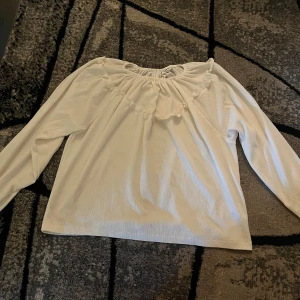 Vit blus med volang från KappAhl - Säljer en söt vit blus från KappAhl i storlek 158/164. Blusen har långärmade puffiga ärmar och en rundad hals med volangdetaljer framtill. Materialet är lätt och har en skön struktur som ger en chill vibe. Perfekt för dig som gillar en enkel men ändå stylish look. En gullig blush som passar till vardagen och till skolan.😊