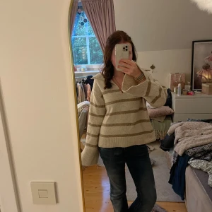 Randig beige stickad tröja Gina Tricot - Supermysig stickad tröja från Gina Tricot i beige med breda bruna ränder. Tröjan har v-ringad hals med krage och långa ärmar med ribbade muddar. Passformen är loose och den är perfekt för chill dagar. Materialet är mjukt och värmande. Perfekt till hösten!🥰🍁🍂OBS! Aldrig använd!Pris kan såklart alltid diskuteras🤗