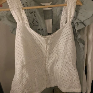 Vit topp - Säljer en söt vit blus med spetsdetaljer och knappar framtill. Har en deffekt- en knapp saknas där fram men ingenting annat! 