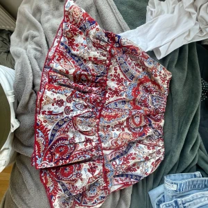 Mönstrad kjol i rött och blått - Säljer en färgglad kjol med ett livligt mönster i rött, blått och vitt. Kjolen har en omlott-design och är kort, perfekt för varmare dagar. Den har en bekväm passform och är tillverkad i ett lätt material.