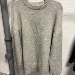 Grå stickad tröja - Säljer en stilren grå stickad tröja med rund hals och långa ärmar. Perfekt för kyligare dagar och enkel att matcha med olika outfits. Fungerar även nu på våren för dig som vill bära väst.