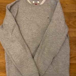 Grå sweatshirt från Tommy Hilfiger - Säljer en stilren grå sweatshirt från Tommy Hilfiger med rund hals och diskret logga på bröstet. Riktigt skön tröja som är perfekt för en avslappnad look.