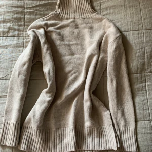 Beige stickad polotröja - Säljer en mysig beige stickad polotröja med ribbade detaljer vid krage, ärmslut och nederkant. Perfekt för kyliga dagar och ger en stilren look. Passar bra till både jeans och kjol.