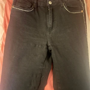 Svarta flare  jeans med kontrastsömmar - Snygga svarta jeans med vita kontrastsömmar runt fickorna och stygnet generelt. Klassisk femficksdesign och knappgylf. Perfekta för en stilren look. Köpta för 400 i Missay, använd endast 3 gånger och inga defekter!! Storlek 38 men väldigt stretchiga 